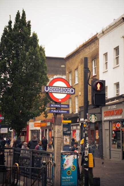 A black and white image of Bethnal Green Tube Station platform showing a man walking away from the camera, dressed in dark clothing and carrying a small bag. The station has a curved, tunnel-like ceil